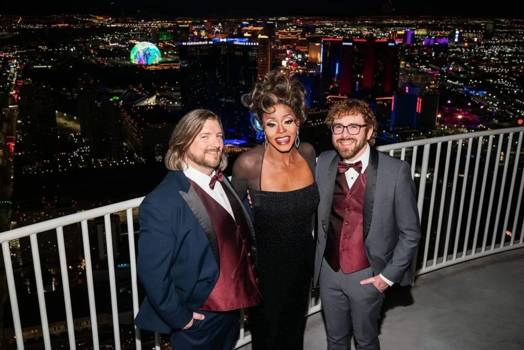 Toni James standing with two people in formalwear against the Las Vegas skyline at night